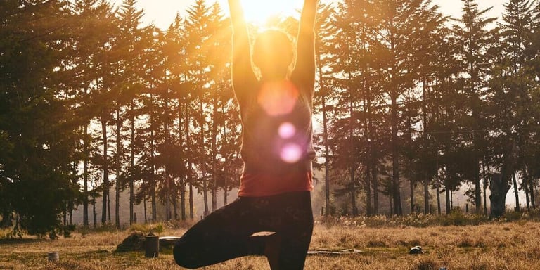 Kvinna som stretchar i naturen med solen skinandes på henne.